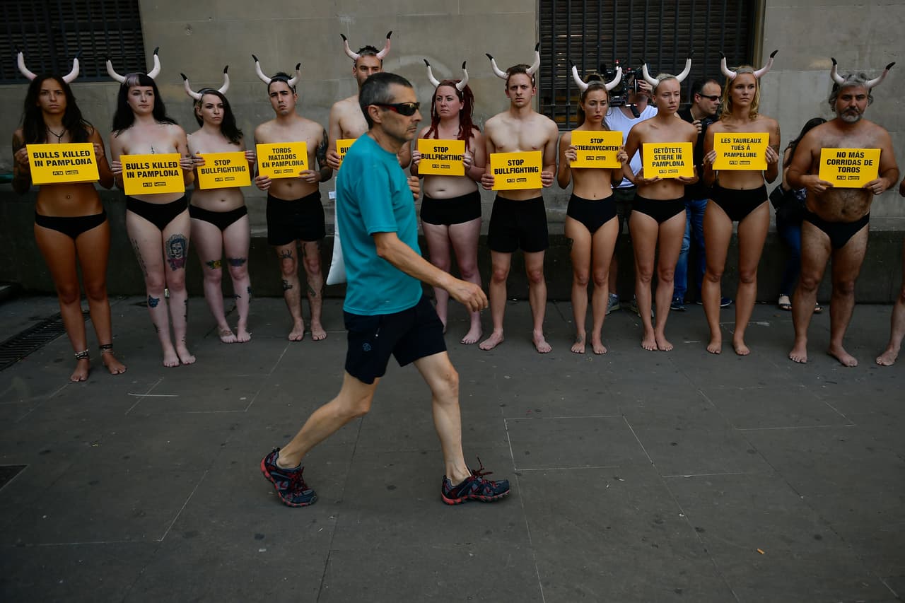 Un hombre pasa justo frente a una docena de hombres y mujeres que muestran mensajes de protesta contra el uso de los toros en esas actividades recreativas.
<br>