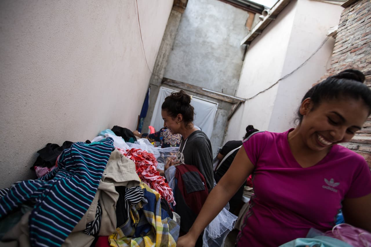 <b>Un par de mujeres centroamericanas en el albergue Embajadores de Jesús se ríen tras probarse un velo de novia.</b> Cada semana, Banda recibe donaciones de ropa y permite que los migrantes puedan escoger las prendas que necesiten para sus hijos y esposos. Entre las 250 personas que este espacio recibe cada semana, 90% está bajo los MPP o 'Remain in Mexico', que los obliga a esperar de ese lado de la frontera por sus fechas de corte y la resolución de sus casos de asilo.