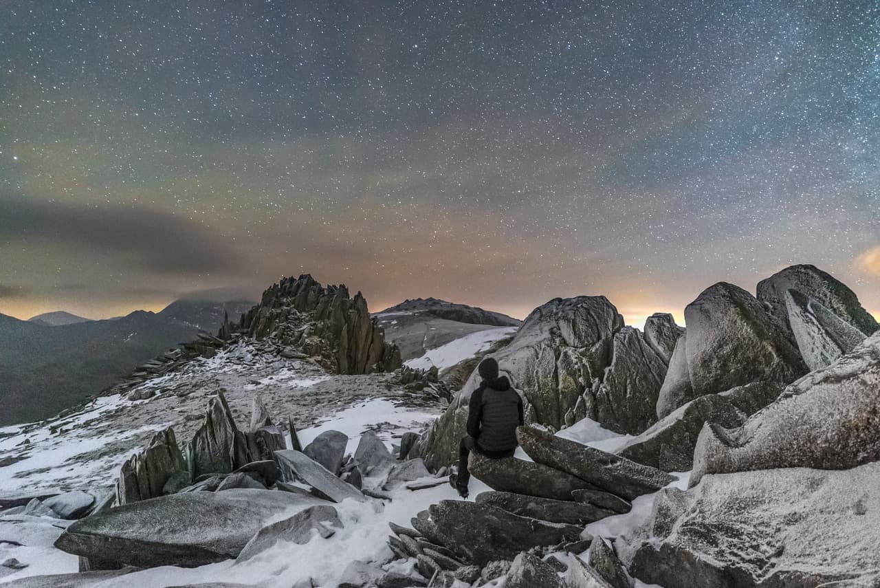Paisaje lunar helado. Un hombre mira las estrellas desde la cima helada del ‘Castillo de los Vientos’ en la montaña Glyder Fach al norte de Gales en medio del invierno.