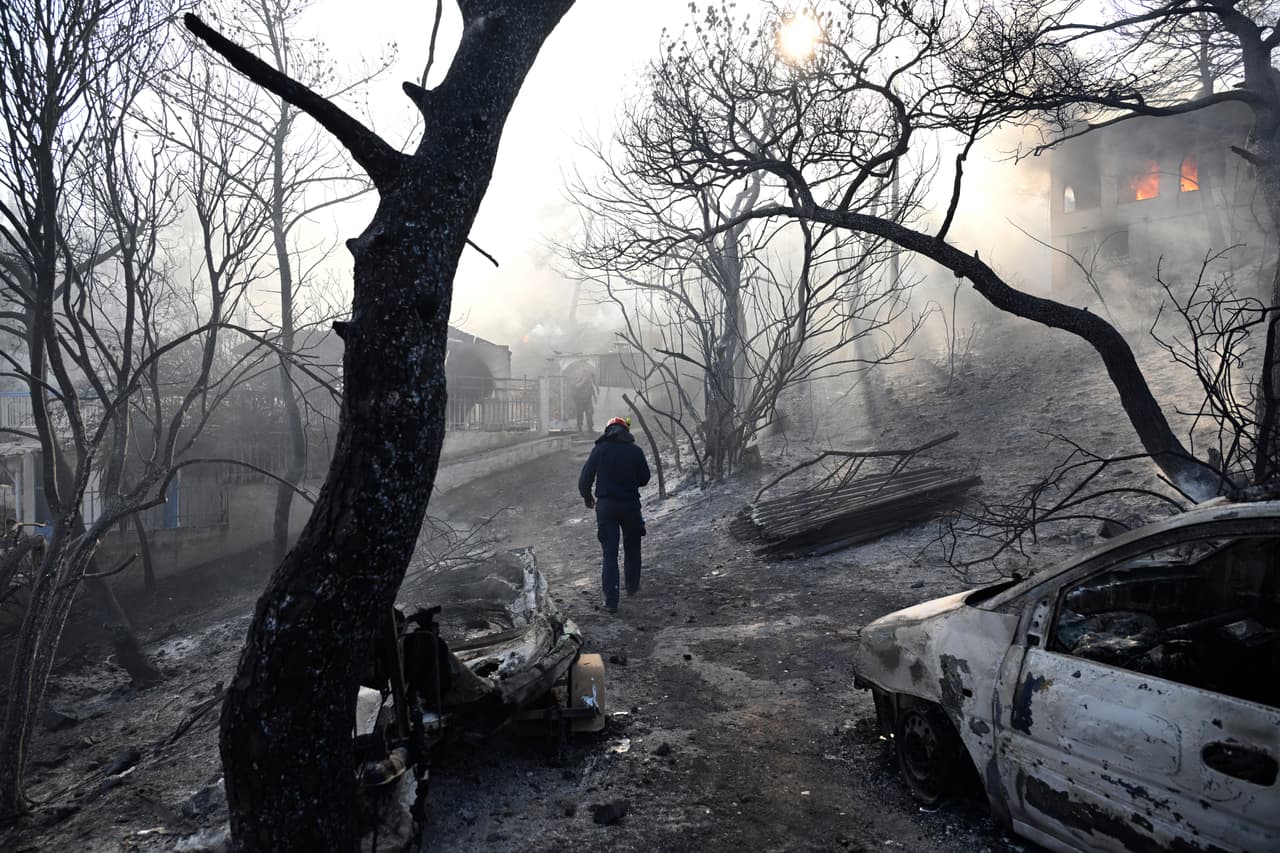 Un bombero camina por una zona quemada mientras las llamas envuelven una casa durante un incendio forestal en la isla de Salamina, al oeste de Atenas, Grecia, el domingo 16 de agosto de 2026.
