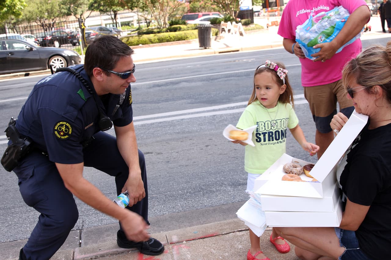 Una pequeña regala una dona a un policía de Dallas. Su padre le ha dicho que hoy se necesitan muchas sonrisas y mucho amor para repartir en esta ciudad.