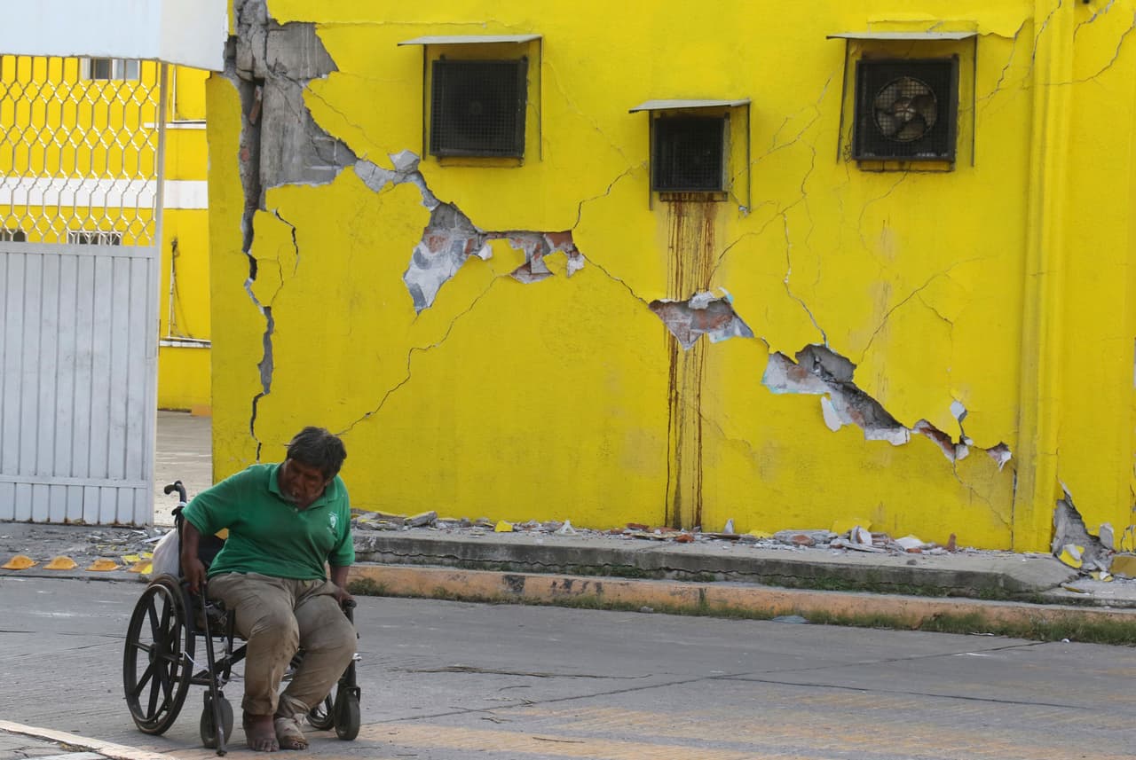 Un hombre avanza con su silla de ruedas frente a una vivienda dañada por el sismo, en Juchitán, Oaxaca.