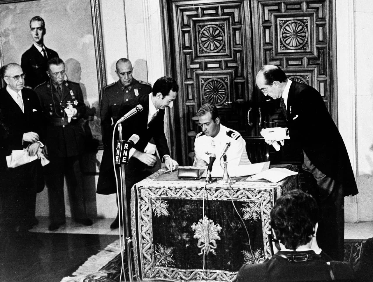 <b>Francisco Franco nombra sucesor</b>
<br>
<br>“Caudillo de España” desde su triunfo sobre la República en 1939, Francisco Franco decidió que era hora de ordenar la sucesión y sobrevivencia de su régimen restableciendo completamente la monarquía. Para eso 
<b>nombró sucesor al trono a Juan Carlos, hijo de Juan de Borbón, quien era el aspirante legal a la sucesión tras la muerte de su padre Alfonso XIII,</b> el rey que depuesto con la proclamación de la República en 1931. Aunque se suponía que la intención eventual de Franco era reponer la monarquía, sus relaciones con Don Juan nunca fueron buenas, aparentemente porque le parecía demasiado liberal y un riesgo para su legado político. 
<b>Las Cortes, que respondían a los deseos del Caudillo, aprobaron el 22 de julio la designación de Juan Carlos,</b> quien pasó a tener el título de Príncipe de España (y no de Asturias, como manda la tradición).
<br>