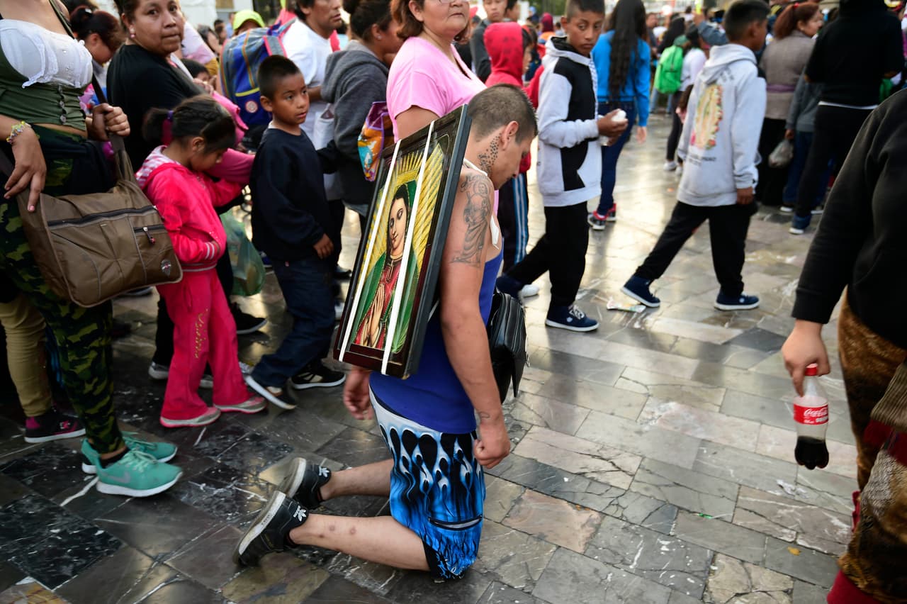 Un peregrino camina de rodillas con un cuadro de la Virgen sobre sus hombros.