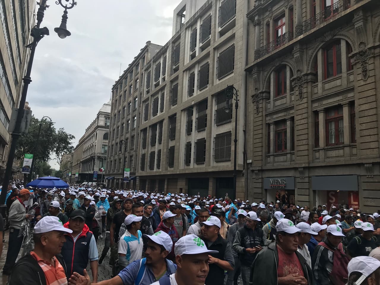 Un grupo de personas camina por calles aledañas al Zócalo de la ciudad con una gorra del gobierno de la Ciudad de México como distintivo.