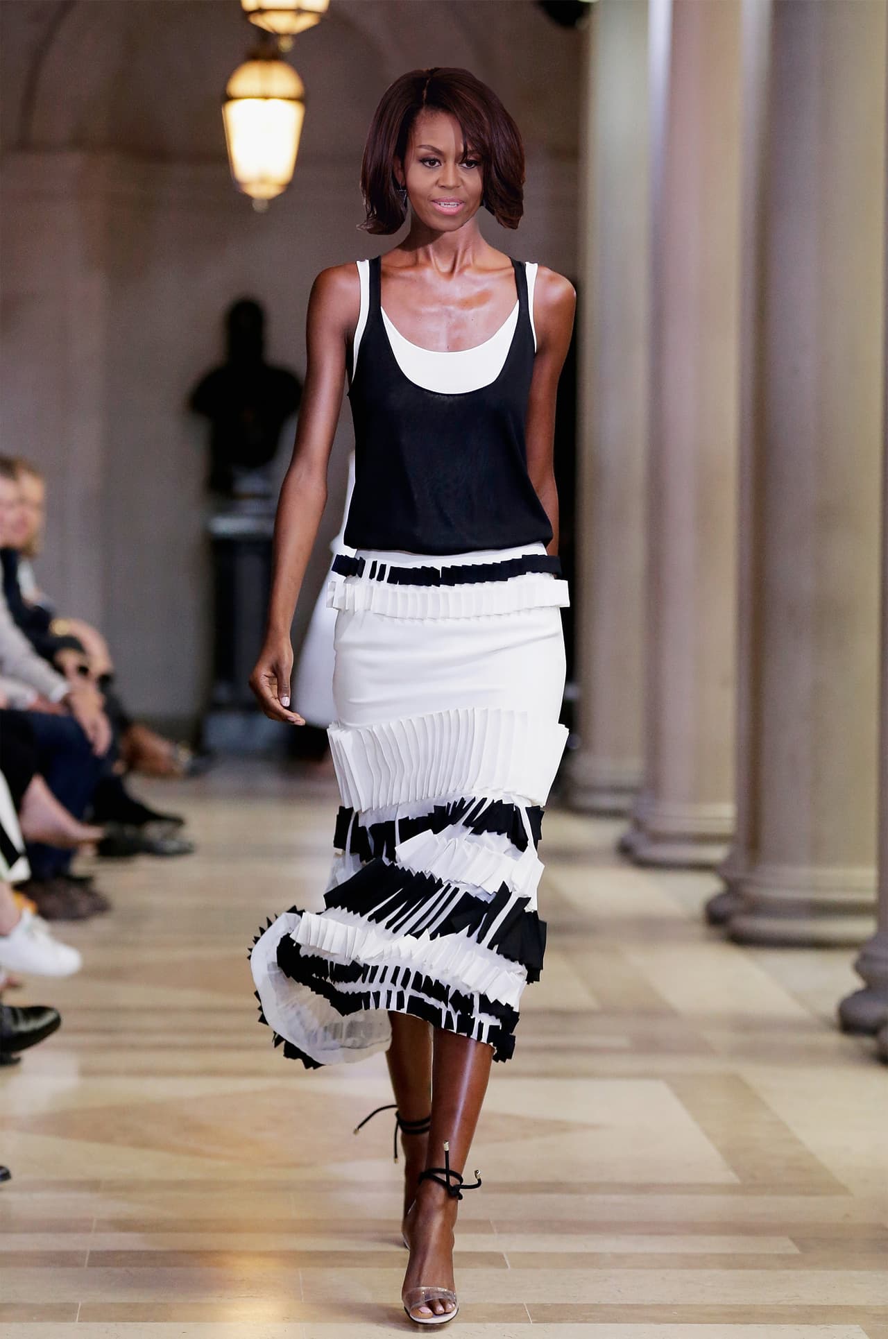 Este traje de dos piezas en blanco y negro de la colección primaveral de 2016 de Carolina Herrera parece que hubiera sido creado para Michelle Obama, y, que de hecho, lo hubiera desfilado. Lucen perfectas en ella este tipo de proporciones, el cuello descotado, los brazos desnudos y una falda que celebra el movimiento y la deja ver poderosa y siempre femenina.