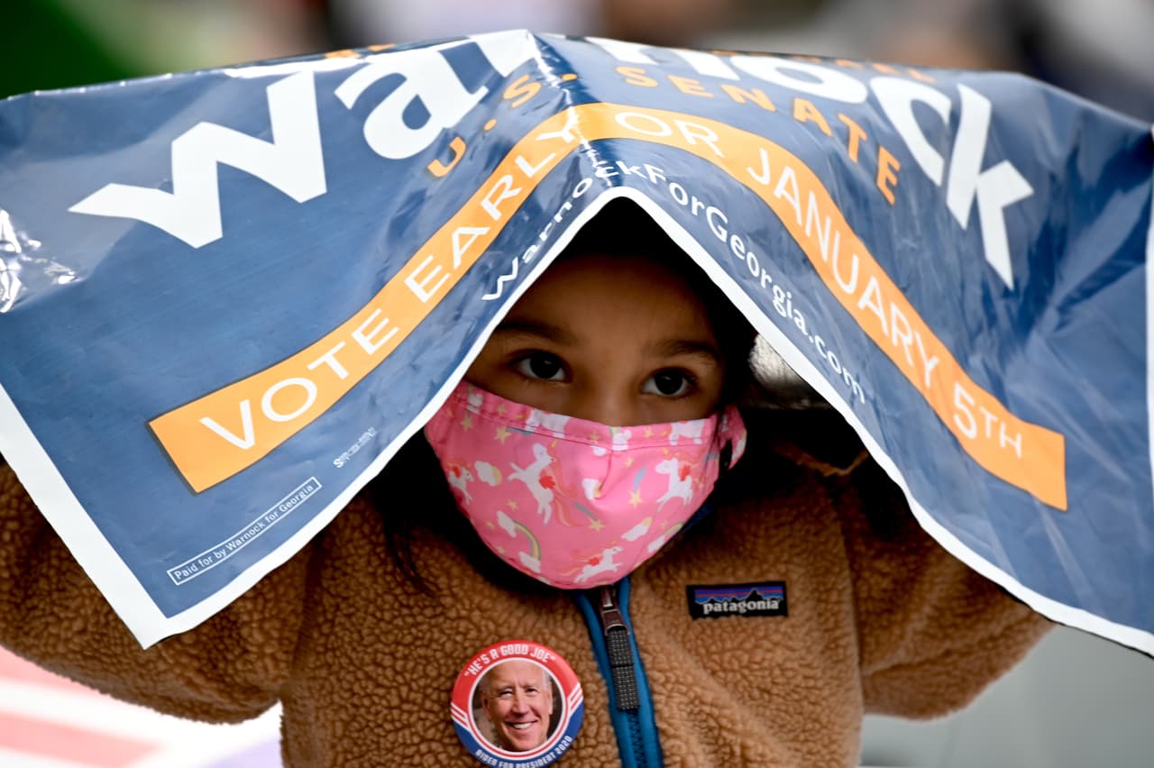 Una niña mira desde debajo de un cartel de campaña mientras observa a los candidatos demócratas al Senado hablar durante un mitin de campaña en Atlanta, donde el presidente electo de Estados Unidos, Joe Biden, hizo campaña por los candidatos demócratas al Senado Jon Ossoff y Reverendo Raphael Warnock y pidió a los residentes el voto porque los necesita en Washigton.