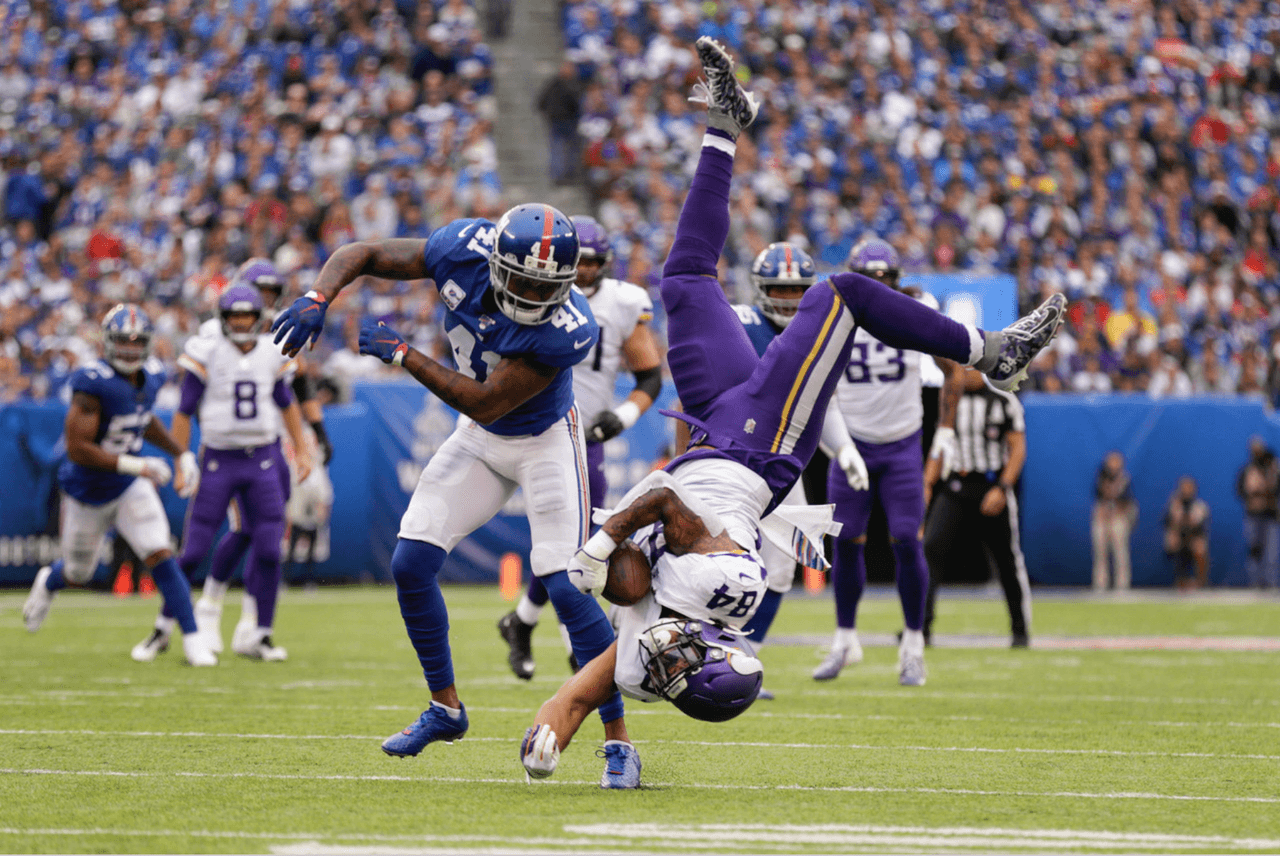 Irv Smith de los Minnesota Vikings atrapa el ovoide mientras hace una pirueta en el aire sobre Antoine Bethea de los New York Giants.