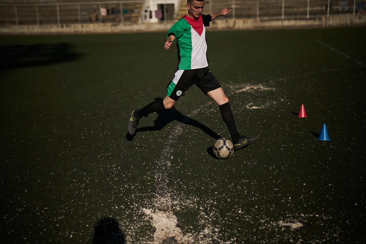 Un joven de una academia de fútbol local, con una camiseta con los colores de la bandera palestina, patea un balón durante una sesión de entrenamiento en un campo de fútbol municipal desgastado en la ciudad de Nablus, en Cisjordania, el jueves 7 de mayo de 2026. (Foto AP/Leo Correa)