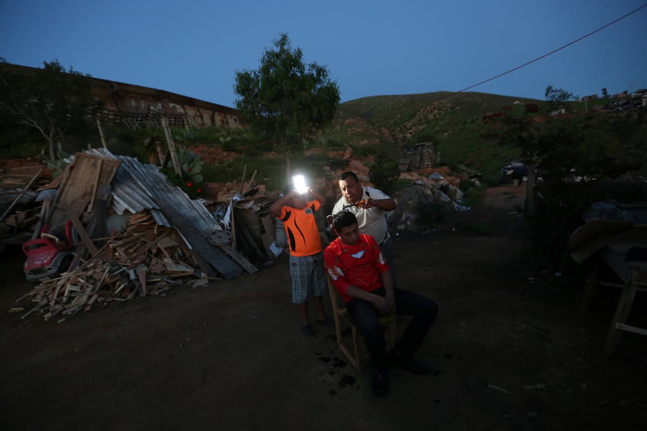 Porfirio, un carpintero de 68 años, corta el cabello de su hijo frente a su casa en la fronteriza Tijuana.