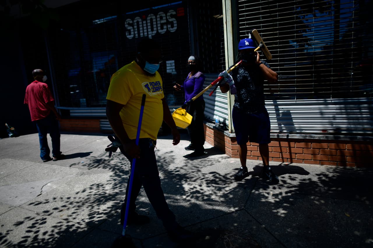 Voluntarios limpian los graffitis en las vitrinas de varios locales comerciales en Filadelfia.Otros colocaron láminas de madera para evitar volvieran a entrar a los negocios ya vandalizados durante las manifestaciones del sábado y domingo.