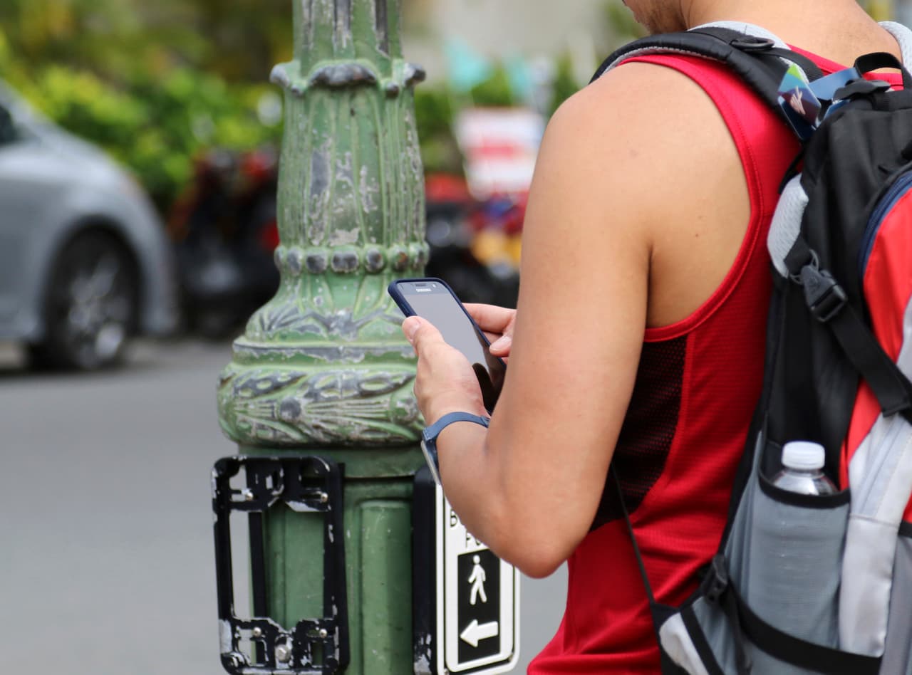 In this Wednesday, Oct. 25, 2017, photo a man uses his cellphone before crossing a street in Honolulu. A new Honolulu ordinance allows police officers to issue tickets to pedestrians caught looking at a cellphone or electronic device while crossing a city street. (AP Photo/Caleb Jones)