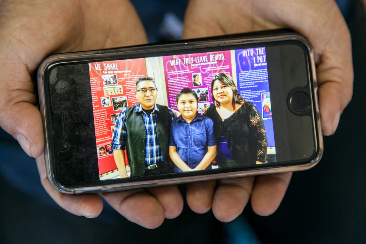 Maty llegó a EEUU en 2003. Era la menor de 12 hermanos y quería buscar mejores oportunidades económicas y ayudar a su familia. Su esposo, Víctor C., que hoy tiene 40 años, llegó años antes, a principios de los 90, huyendo de la violencia de la guerra en Guatemala. Según el relato de Maty, en la época de Efraín Ríos Montt, el ejército mató al papá y otros familiares de Víctor. En la foto, Maty sostiene su teléfono con una foto en la que está en una exposición de un centro comunitario con su esposo Víctor y su hijo Jimmy.