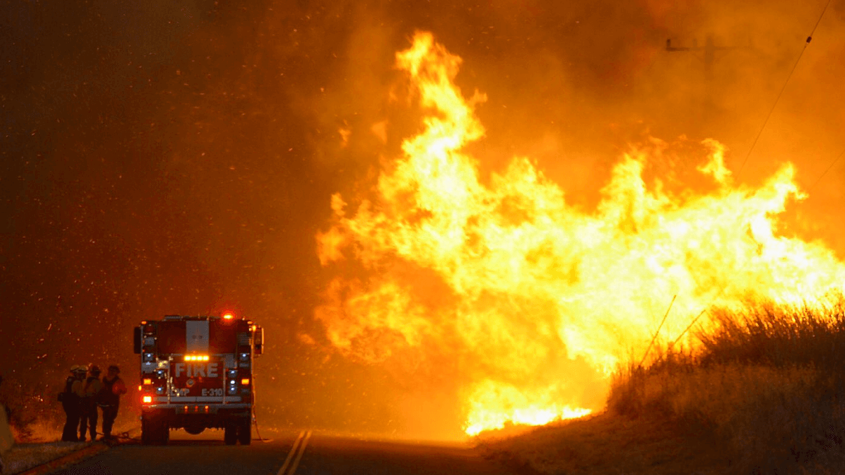 Bomberos se resguardan de las llamas detrás de una unidad de rescate.