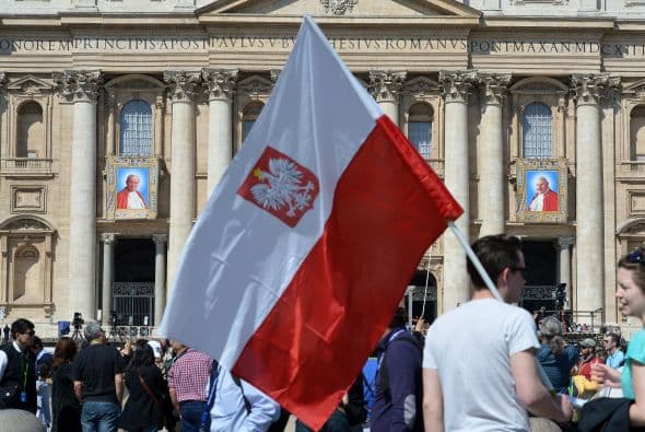 Un hombre sostiene una bandera polaca frente a los tapices de los papas que serán canonizados el 27 de abril.
