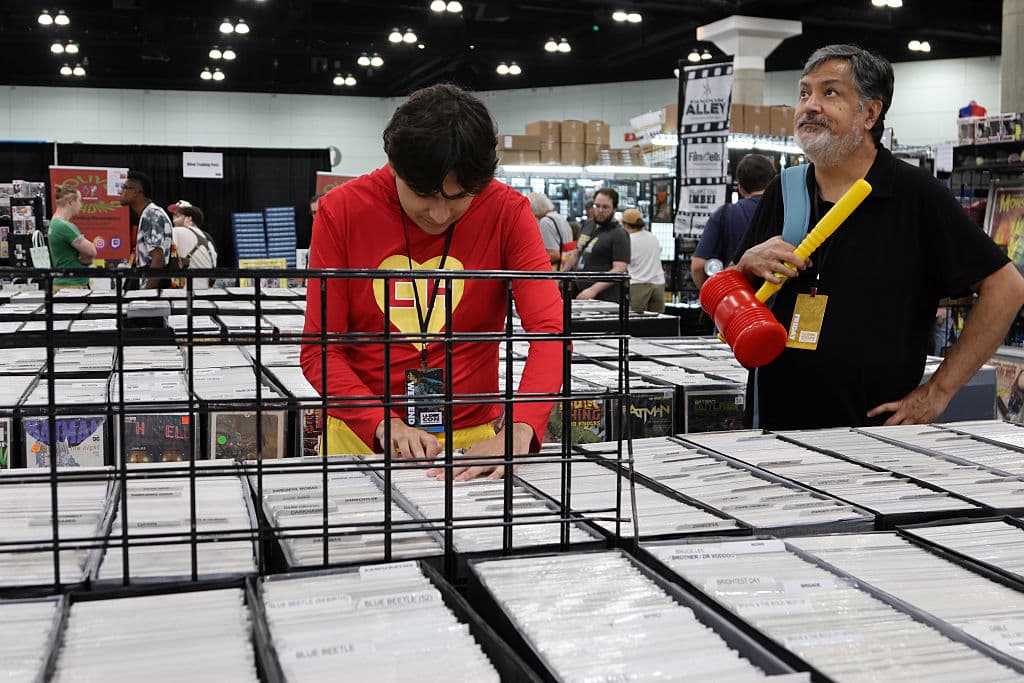 Asistentes, uno de ellos vestido de El Chapulín Colorado, exploran tesoros de papel en LA Comic Con 2025: fans hojean cuidadosamente comics clásicos y nuevas ediciones en el Convention Center.