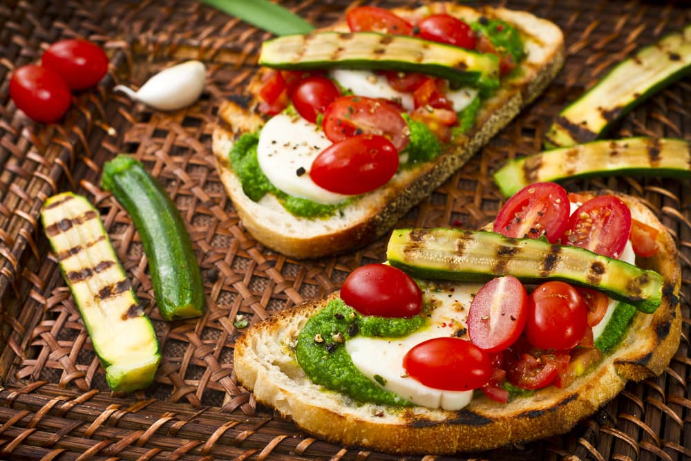 Coloca las rebanadas de pan integral y unta la mayonesa a tu gusto, después ve agregando cada uno de los ingredientes; las hojas de rúcula, las rebanas de zucchini, los tomates cherry y para finalizar la albahaca. Verás que el toque de este último ingrediente aportara su sabor característico haciendo que este sandwich se sienta como recién salido de una cocina del Mediterráneo.