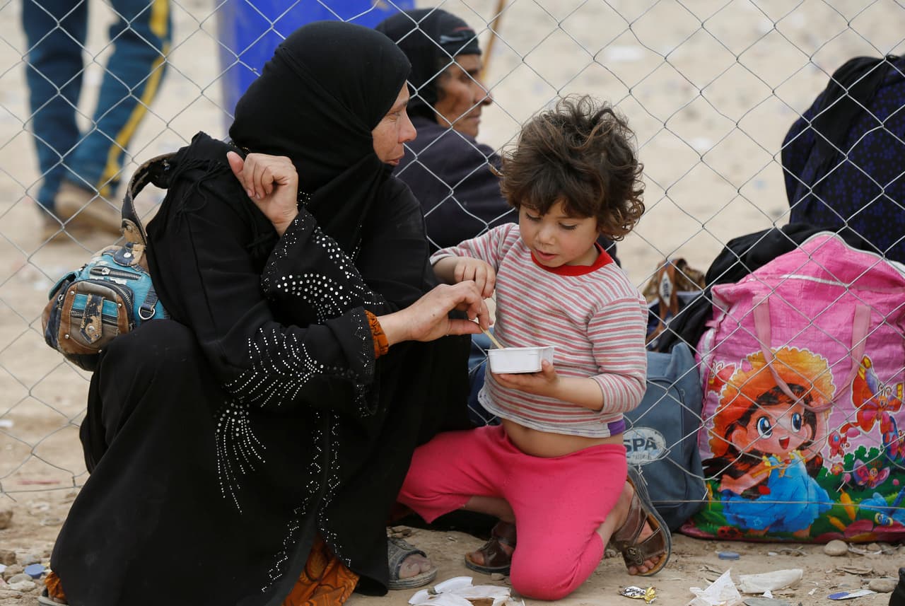 Una madre da de comer a su hija al llegar al campamento en Hammam al-Alil.