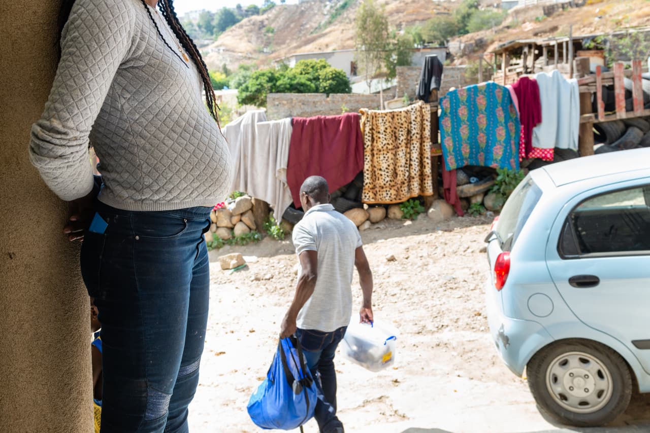 Daniela Pierre mira a su esposo cuando se lleva la ropa para lavarla. Huyó de Haití a Venezuela hace cuatro años después de que la economía colapsó pero la agitación política en el país suramericano la obligó a seguir moviéndose. Contó que pasó cuatro meses viajando en autobús y caminando hasta que llegó a la frontera de EEUU. Ha estado viviendo en el refugio de Tijuana durante tres meses, mientras evalúan su solicitud de asilo.