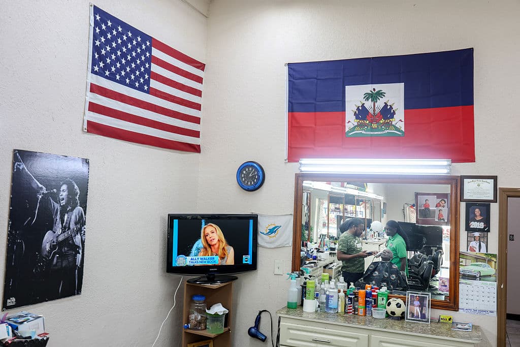 Una fotografía del cantante jamaiquino Bob Marley (1945-1981), la bandera de Estados Unidos y la bandera de Haití con un televisor encendido en esta barbería de Pequeño Haití.