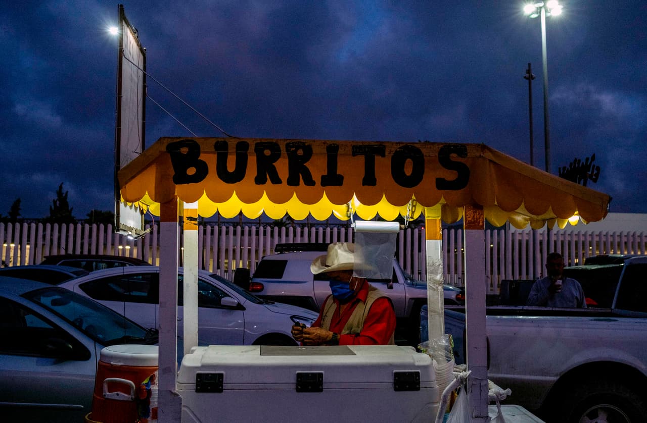 Un vendedor ambulante protegido con una máscara espera clientes cerca de la fila de autos que espera en el cruce de Otay Mesa. El acuerdo, en el que también participó Canadá, mantendrá cerradas las fronteras compartidas a viajes no esenciales hasta el 21 de junio.
<br>