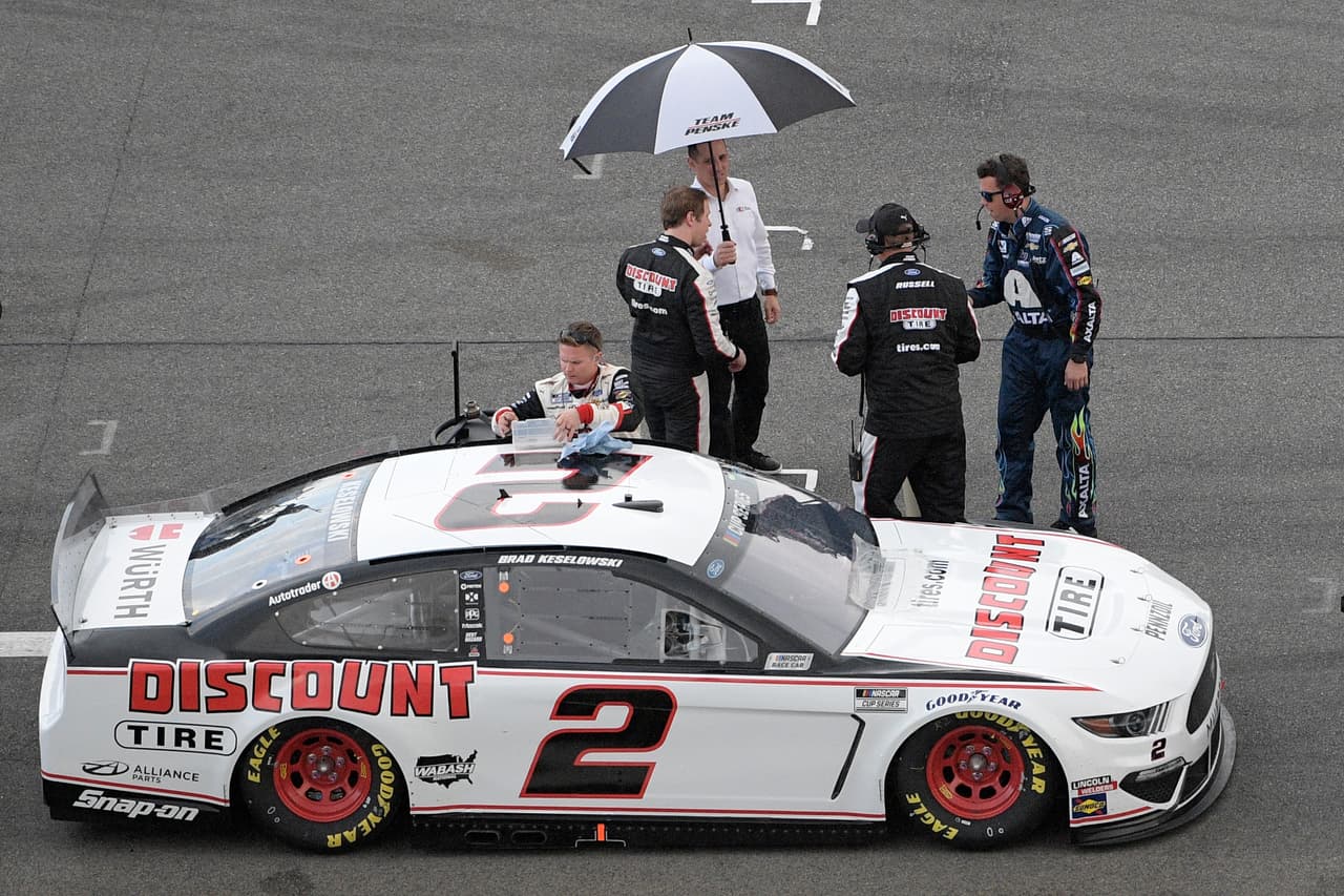 Brad Keselowski, conductor de Mustang para el equipo Penske, se resguarda bajo una sombrilla luego de que la lluvia comenzara a caer en Daytona. La carrera finalmente fue fijada para el lunes a las 4:00pm, luego de que fuera pospuesta temporalmente en dos ocasiones mientras esperaban que escampara.