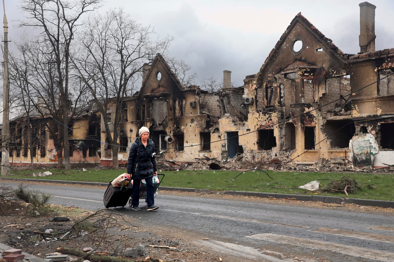 Una mujer con sus pertenencias el viernes 8 de abril de 2022 frente a casas dañadas durante un combate en Mariupol, Ucrania.