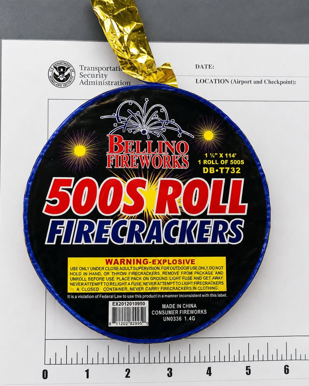 Rollo circular de petardos "Bellino Fireworks" de 500 tiros sobre un formulario oficial de la TSA, con etiquetas de advertencia explosiva y una cinta dorada brillante arriba.