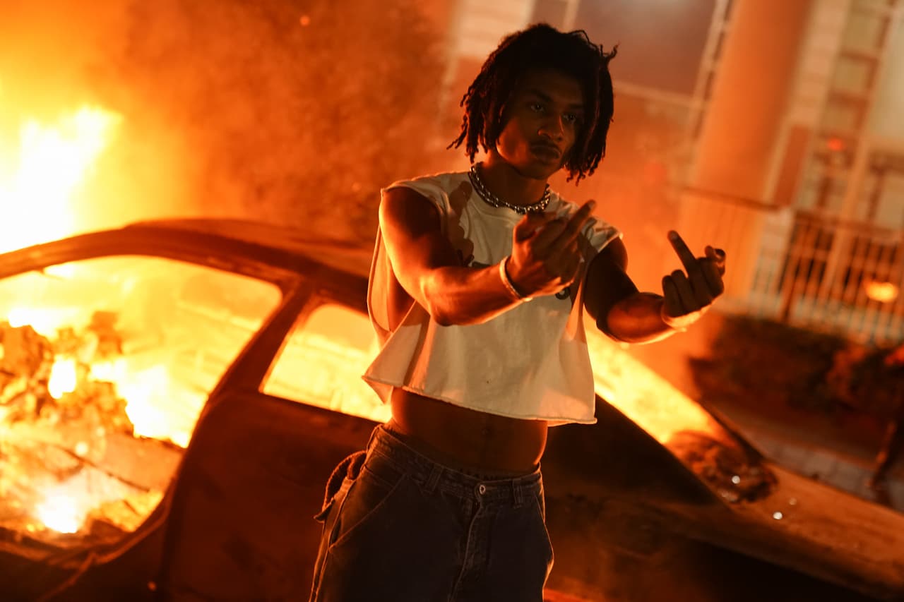 Un hombre posa frente a un auto en llamas durante una protesta el 29 de mayo de 2020 en Atlanta, Georgia.