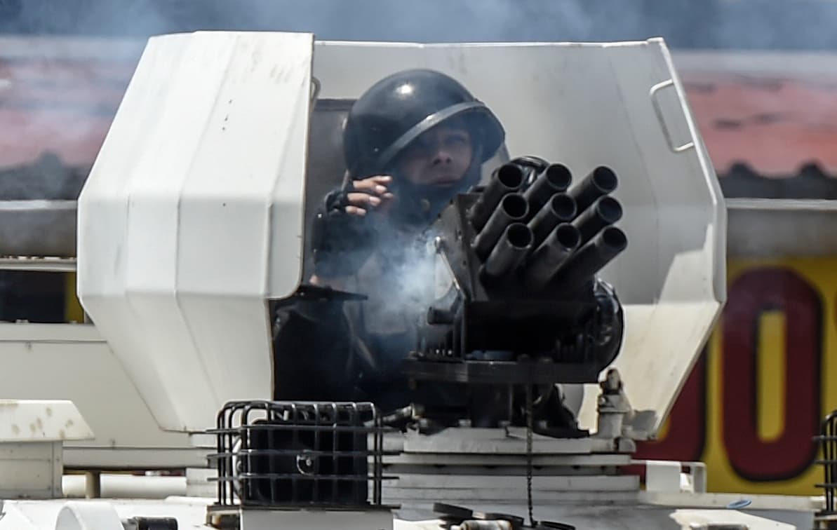 Un policía lanza bombas de gas lacrimógeno a los manifestantes desde un tanque antimotines.