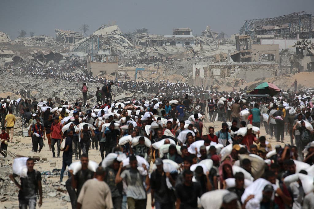 Palestinos caminan con sacos de harina cerca de Jabalia, en el norte de la Franja de Gaza, el 27 de julio de 2025, después de que camiones con ayuda humanitaria entraran en el norte de Gaza procedentes del paso fronterizo de Zikim. Aviones jordanos y emiratíes dejaron caer alimentos en Gaza el 27 de julio, cuando Israel inició una "pausa táctica" limitada en sus operaciones militares para permitir que la ONU y las agencias de ayuda humanitaria abordaran una crisis de hambre cada vez más grave.