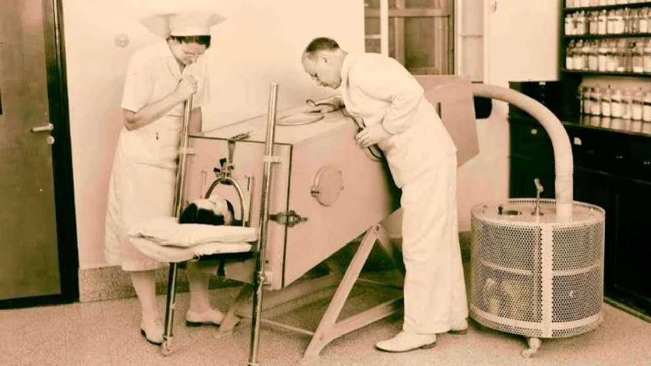 Un doctor, con ayuda de una enfermera, atiende a un niño dentro de un "Pulmón de Acero". Según algunos reportes, podría tratarse de Paul Alexander.