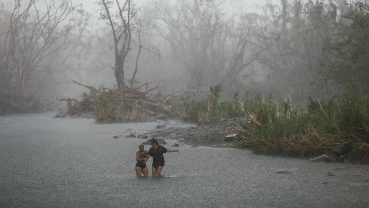 Personas cruzan el río Espíritu Santo en Río Grande (norte) durante las torrenciales lluvias que afectaron a Puerto Rico a casi tres semanas de azote del huracán María.