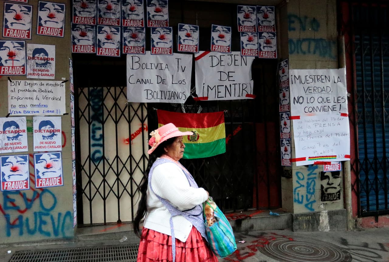 Una boliviana pasa frente a las instalaciones de la televisión estatal boliviana y la estación radial Radio Patria Nueva luego de que fueron cerradas por manifestantes que pedían la renuncia de Morales. Tras casi tres lustros en el gobierno, Morales llegó con la popularidad mermada a los comicios para optar por un cuarto mandato. Escándalos de corrupción, su afán de reelegirse a pesar de un referendo que le negó esa posibilidad y acusaciones de autoritarismo, debilitaron su capital político a pesar de su buena gestión económica que condujo al país andino hacia el crecimiento con baja inflación.