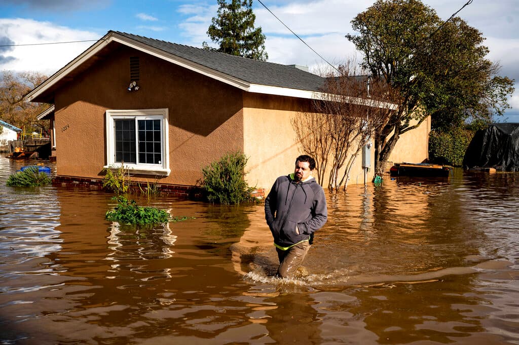 Nick Enero, con el agua por las rodillas, camina por una calle inundada en Montecito. Más de la mitad de los 58 condados de California fueron declarados zona catastrófica, refirió el gobernador Newsom.