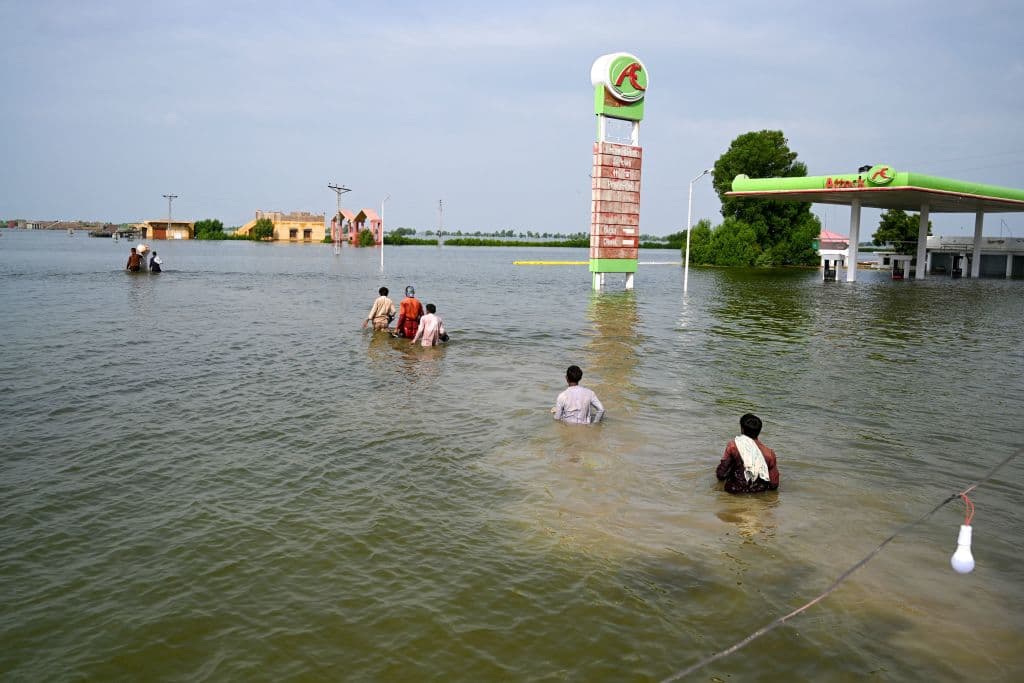 Internally displaced people wade through floodwaters to return home after heavy monsoon rains in Dadu district, Sindh province on September 7, 2022.