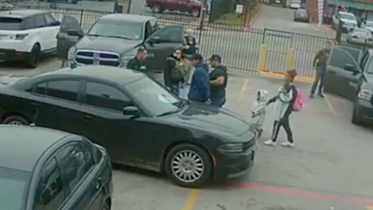 Una mujer con un bebé en brazos y un niño cruzan la calle y llegan a donde tenían al hombre arrestado. Se desconoce el parentesco entre ellos.