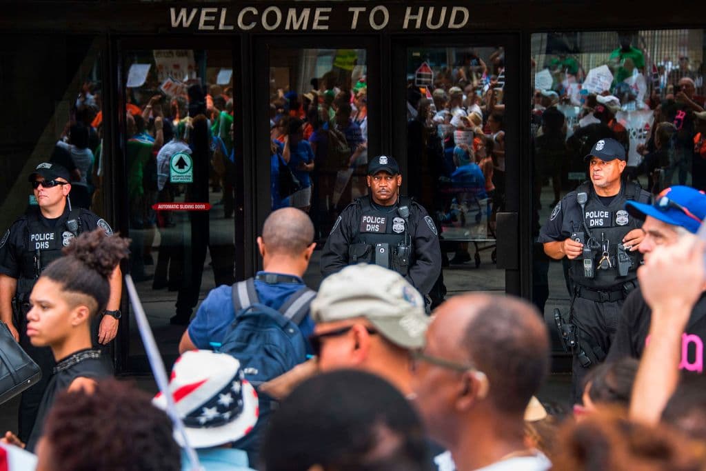 Security stands guard outside the Department of Housing and Urban Development as demonstrators march past with low-income tenants, housing advocates and community leaders from across the country protesting the Trump administration's "proposed billions in cuts to federal housing programs" in Washington, DC, on July 12, 2017. / AFP PHOTO / JIM WATSON (Photo credit should read JIM WATSON/AFP/Getty Images)