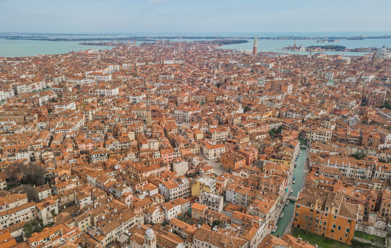 <b>Venecia</b>
<br>
<br>Desde el aire se aprecia la forma de pez de esta peculiar ciudad italiana, atravesada por canales y calles estrechas.
<br>
<br>Si se sienta a la derecha del avión verá desde las barreras contra inundaciones hasta la vecina isla Lido, también apreciará desde arriba los techos de terracota, los viejos campanarios y el Gran Canal. En los últimos segundos del vuelo se ven las islas Burano y Torcello, iconos de Venecia.
<br>