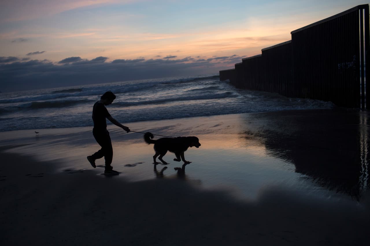 Un hombre pasea su perro cerca de la valla fronteriza en la playa de Tijuana, México. 4 de marzo de 2017.