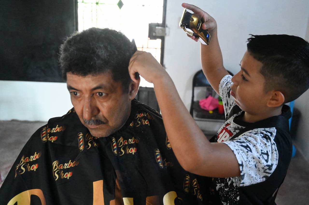 En la foto, Eduardo Espinal, un niño de 12 años que corta el cabello a un cliente en su barbería en Comayagua, Honduras. Con tijeras y afán de superación, este niño se abre camino con su barbería en Honduras para escapar de las dificultades económicas y del 'sueño americano'.
