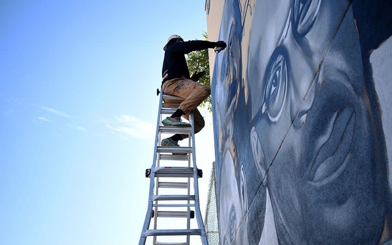 “Empecé en el arte aquí en Arizona”, dice el muralista Just Dixon, “y me fui porque no había artistas negros ni nadie con quien realmente pudiera conectarme”. Trabaja en su segundo mural para el proyecto en la esquina noroeste de las calles Second y Lincoln el 1 de febrero de 2022. Giovannie ‘Just’ Dixon. Ubicación: Esquina noroeste de las calles Second y Lincoln