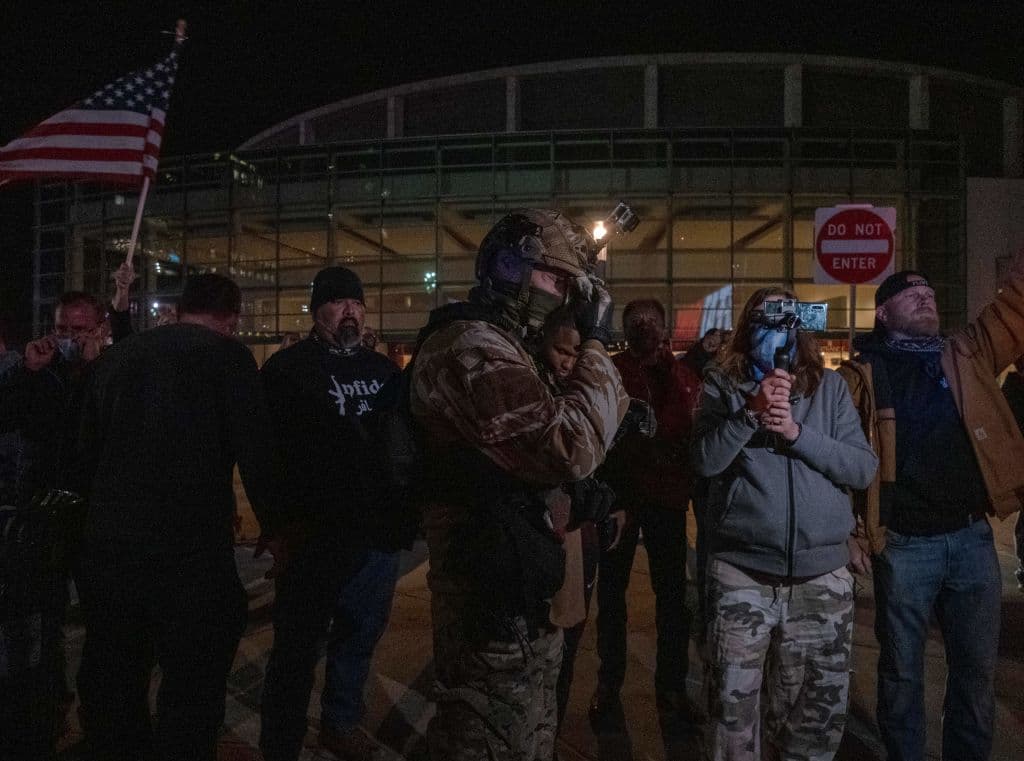 Un partidario del presidente Trump, vestido con traje y equipo táctico, se limpia la cara y se arregla su equipamiento tras una confrontación con manifestantes en Detroit.