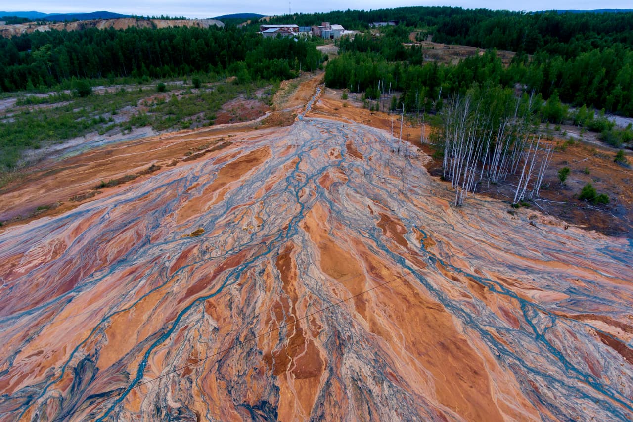 Una vista aérea tomada el 27 de junio de 2020 muestra ríos de color naranja que se despliegan sobre el paisaje boscoso cerca de una mina de sulfuro de cobre en desuso cerca del pueblo llamado Lyovikha en los Urales.