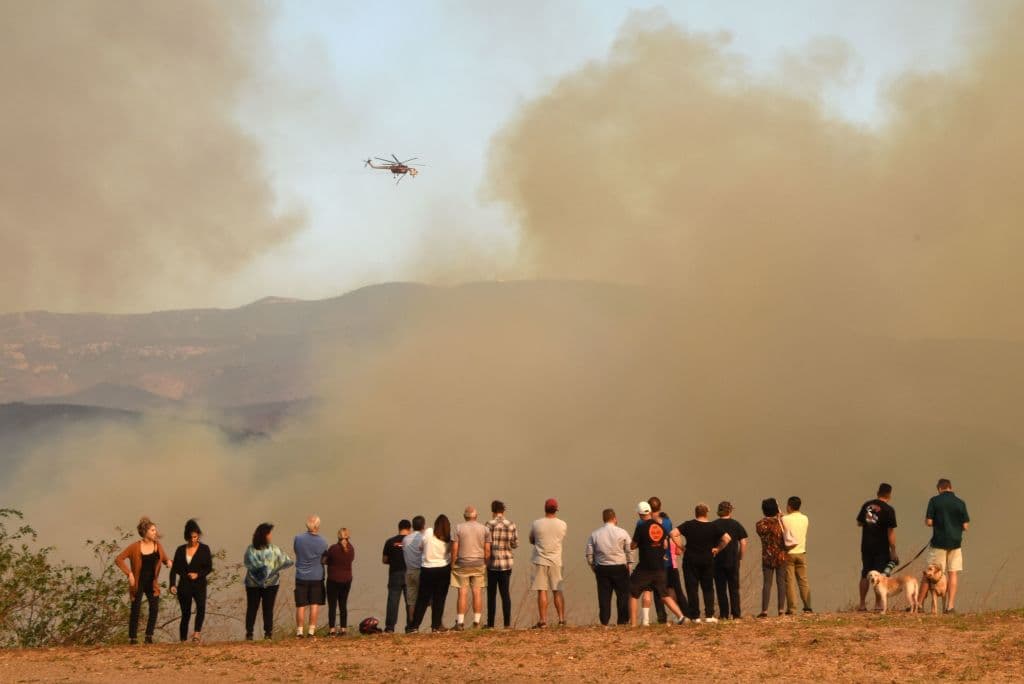 TOPSHOT - People watch water-dropping helicopters amidst smoke from the Canyon Fire 2, October 9, 2017 in Orange, California. / AFP PHOTO / Robyn Beck (Photo credit should read ROBYN BECK/AFP/Getty Images)