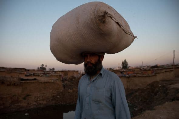 Un hombre afgano , que huyó de su país de origen a Pakistán , camina con una bolsa de paja en la cabeza.