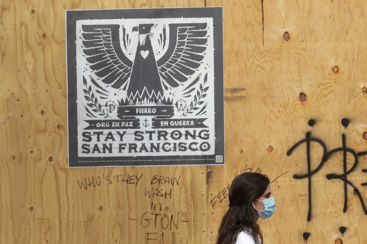 Una mujer camina frente a uno de los muchos negocios que han cerrado sus puertas, donde un artista colocó un cartel en el que se lee "Manténte fuerte, San Francisco".