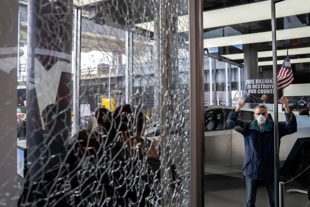 Un manifestante se encuentra dentro de un showroom de Tesla, junto a una puerta destrozada, durante una protesta contra Elon Musk y Tesla, el sábado 1 de marzo de 2025 en Nueva York. (AP Foto/Adam Gray)