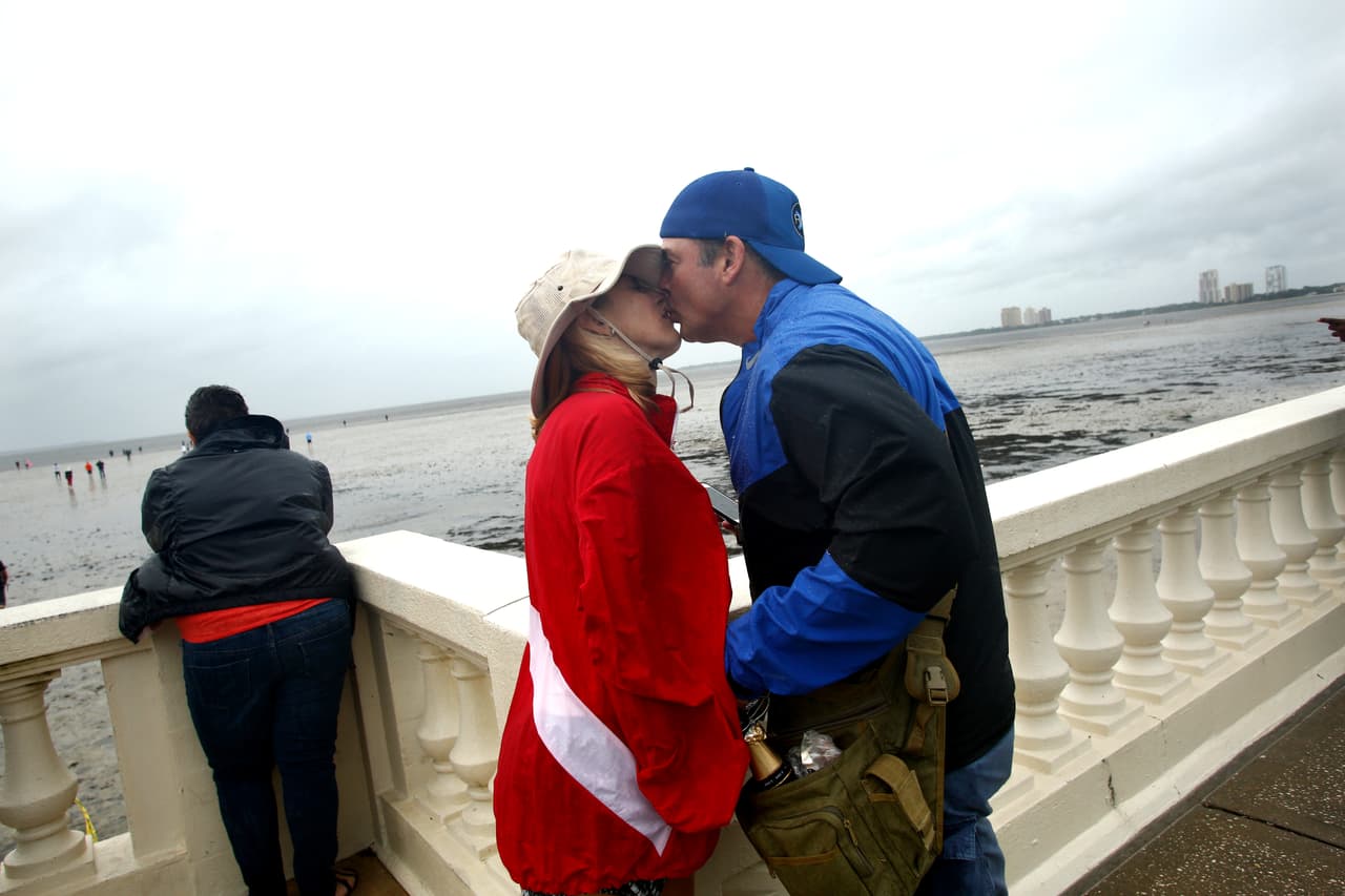 Los residentes de Tampa, John y Daniel Redd, comparten un beso y un poco de champaña mientras se unen a otros para inspeccionar el extremo agua que se aleja en Tampa Bay.