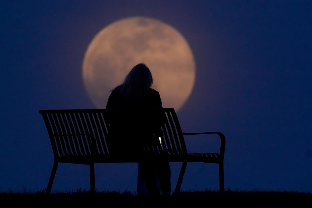 Una mujer sentada en un parque mientras sale la luna en New Albany, Indiana.